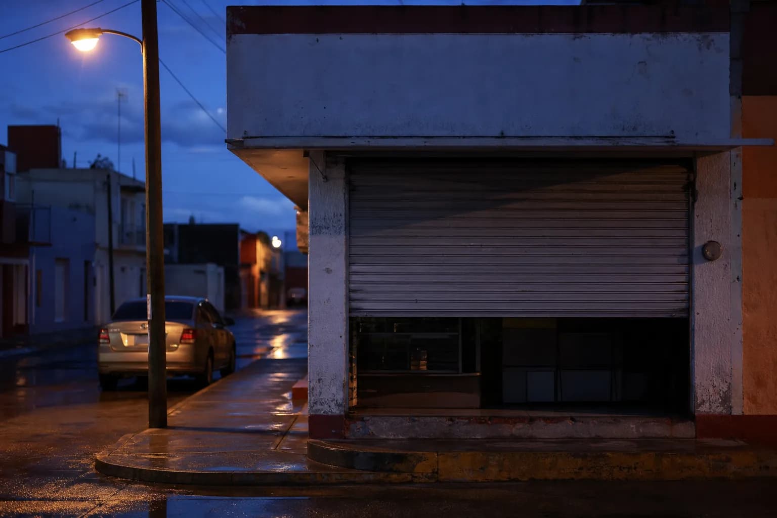 Tienda de noche con la cortina a medio bajar y las luces apagadas.